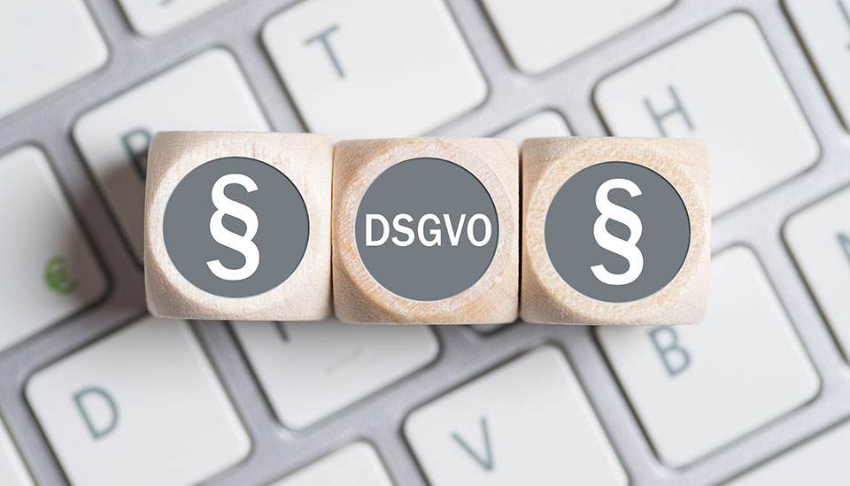 Symbolbild: Drei Würfel liegen auf einer Computertastatur, auf den beiden äußeren Würfeln ist ein Pragraphenzeichen abgebildet und auf dem mittleren steht das Wort „DSGVO“