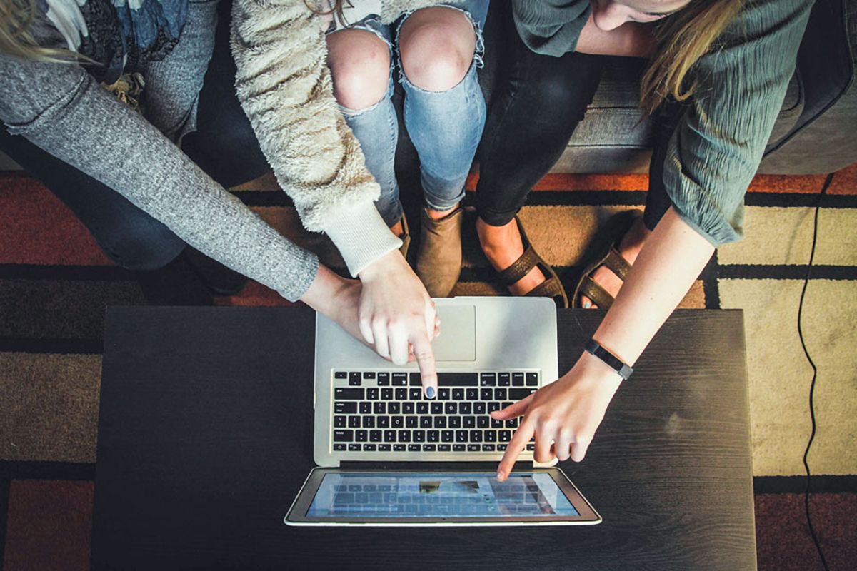 Drei Frauen zeigen auf einen Laptop der auf einem Couchtisch steht (Vogelperspektive)