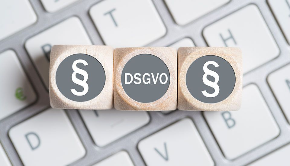 Symbolbild: Drei Würfel liegen auf einer Computertastatur, auf den beiden äußeren Würfeln ist ein Pragraphenzeichen abgebildet und auf dem mittleren steht das Wort „DSGVO“